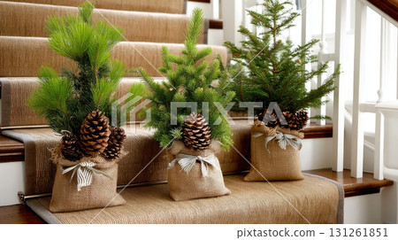 Three small evergreen trees in burlap bags sit on a staircase, adding a festive touch to the home during the holiday season 131261851