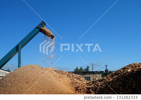 Wooden sawdust pour of chopping machine on heap outdoors at woodworking plant. 131262333