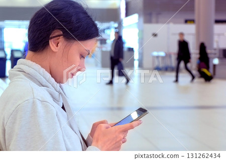 Woman check-in online registration on her mobile phone in airport hall, side view. Woman check-in online registration on her mobile phone in airport hall, side view. 131262434