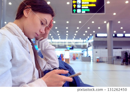 Woman at the airport with a mobile phone in her hands waiting for her flight, side view. 131262450