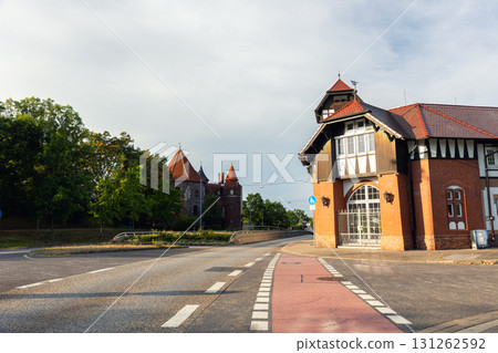 Schleinufer street view in Magdeburg shows brick building with timber elements road intersection, bathed in warm sunlight. Background rise historic towers and castle walls surrounded by green trees Schleinufer street view in Magdeburg shows brick building with timber elements road intersection, bathed in warm sunlight. Background rise historic towers and castle walls surrounded by green trees 131262592