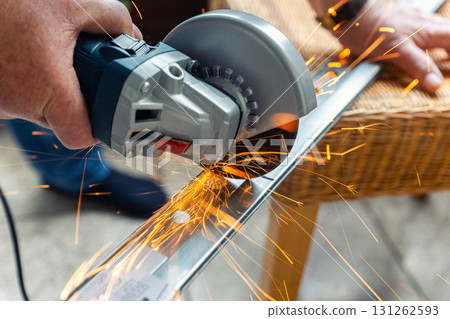 A person is cutting metal with an angle grinder, producing bright orange sparks flying in different directions. The close-up shot captures power, precision and intensity of work 131262593