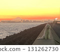A large white dog sitting on a breakwater with the sunset painting the sky red and Mt. Fuji in the background 131262730