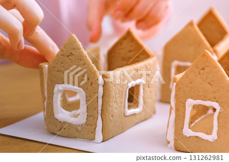 Woman's hands make gingerbread houses glues details with sugar sweet icing. Cooking homemade gingerbread house. Woman's hands make gingerbread houses glues details with sugar sweet icing. Cooking homemade gingerbread house. 131262981