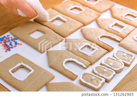Woman's hands decorate with sugar sweet icing cookies for gingerbread houses. Cooking homemade gingerbread house. Woman's hands decorate with sugar sweet icing cookies for gingerbread houses. Cooking homemade gingerbread house. 131262985