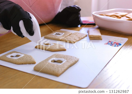 Woman's hands decorate with sugar sweet icing cookies for gingerbread houses. Cooking homemade gingerbread house. Woman's hands decorate with sugar sweet icing cookies for gingerbread houses. Cooking homemade gingerbread house. 131262987
