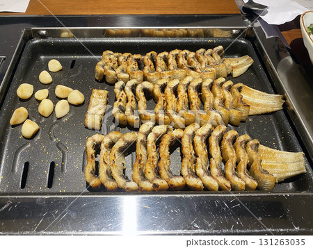 Perfectly grilled Korean eel with roasted garlic on a black grill pan for traditional Korean cuisine Perfectly grilled Korean eel with roasted garlic on a black grill pan for traditional Korean cuisine 131263035
