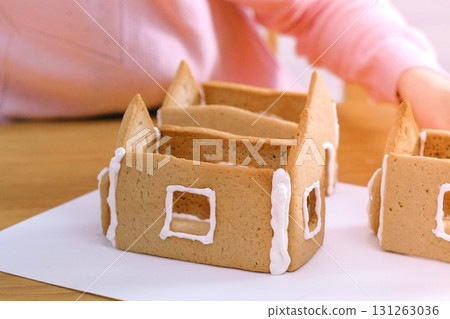 Woman's hands make gingerbread houses glues details with sugar sweet icing. Cooking homemade gingerbread house. Woman's hands make gingerbread houses glues details with sugar sweet icing. Cooking homemade gingerbread house. 131263036
