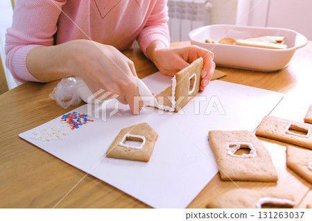 Woman's hands make gingerbread house glues details with sugar sweet icing. Cooking homemade gingerbread house. Woman's hands make gingerbread house glues details with sugar sweet icing. Cooking homemade gingerbread house. 131263037