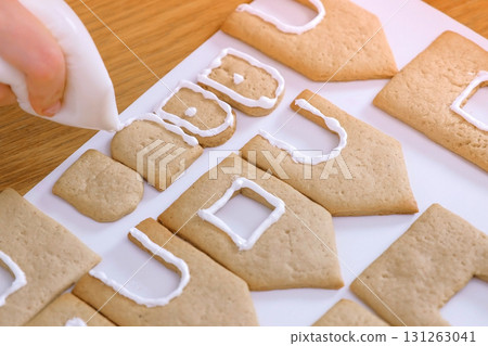 Woman's hands decorate with sugar sweet icing cookies for gingerbread houses. Cooking homemade gingerbread house. 131263041