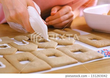Woman's hands decorate with sugar sweet icing cookies for gingerbread houses. Cooking homemade gingerbread house. 131263042