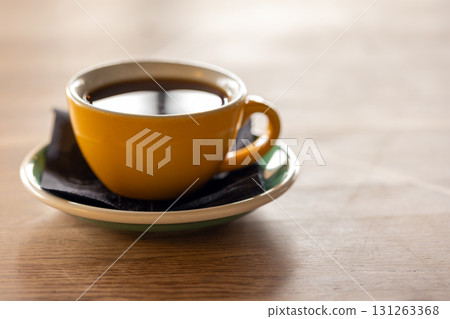 A warm yellow coffee cup sits on a green-rimmed saucer with a black napkin, close up 131263368