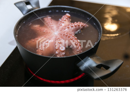 A pink octopus bubbles in simmering water inside a black pot on a glass stove top A pink octopus bubbles in simmering water inside a black pot on a glass stove top 131263376