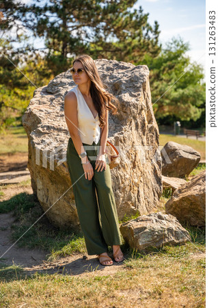 Young woman dressed in white vest and green trousers posing outdoors in Old Money style. Concept of timeless elegance, fashion confidence and classic aesthetic in modern lifestyle. 131263483