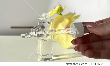 Serum dropper in woman hand with transparent cosmetic liquid and glass bottle on light background with orchid and sunlight. Skincare beauty product Serum dropper in woman hand with transparent cosmetic liquid and glass bottle on light background with orchid and sunlight. Skincare beauty product 131263568