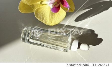 Glass cosmetic dropper with transparent facial serum and bottle on light background with orchid and natural sunlight. Beauty skincare product 131263571