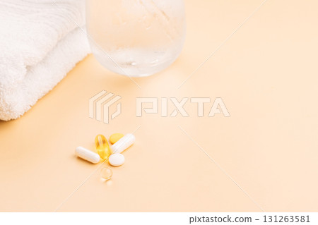 Vitamin pills on beige desktop with towel and dewy glass simple self care scene Vitamin pills on beige desktop with towel and dewy glass simple self care scene 131263581