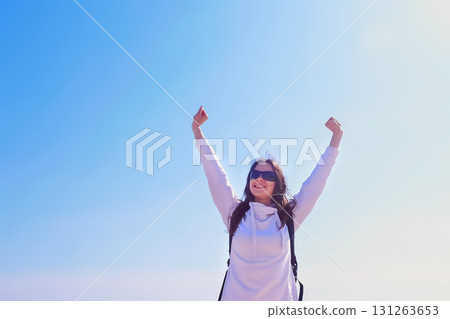 Happy girl winner in victory pose with raising hands on blue sky background. 131263653