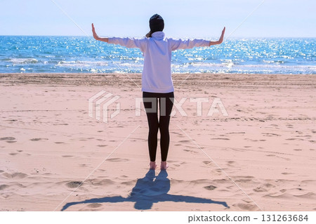 Woman stands on sand sea beach arms out to sides makes yoga exercise back view. Woman stands on sand sea beach arms out to sides makes yoga exercise back view. 131263684
