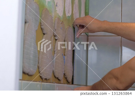 Man tiler making renovation repair at home, removes tiles from wall in toilet. Man tiler making renovation repair at home, removes tiles from wall in toilet. 131263864