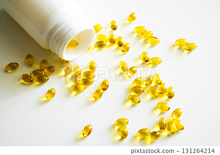 Golden fish oil capsules spilled from white plastic bottle on clean white background Golden fish oil capsules spilled from white plastic bottle on clean white background 131264214
