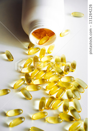 Golden capsules spilled from white plastic bottle on white surface in bright light 131264226