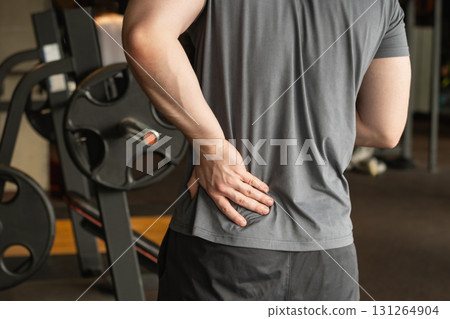 Athlete or young sporty man standing with pain in lower back at gym with muscle tension. Arm, inflammation or exercise with discomfort at fitness center. 131264904