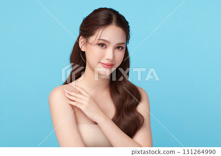 A beautiful young Asian woman with clean, fresh skin against a blue background. Skincare, facial treatment, cosmetology, beauty, and spa. An elegant portrait of an Asian woman. 131264990