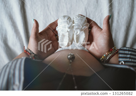 Expectant Mother Holding Baby Shoes Over Belly 131265082