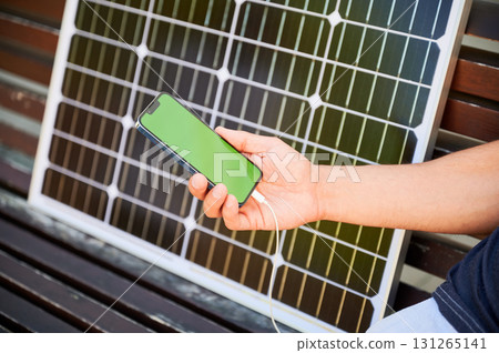 Cropped view of man using smartphone with green screen connected to photovoltaic solar panel. Integration of sustainable renewable energy into life, practical use of solar power for charging devices. 131265141