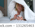bed robe Relaxing woman in a robe using phone on a bed at a cozy hotel room Woman in a white robe using a smartphone while sitting on a bed in a cozy, well-decorated bedroom. 131265463