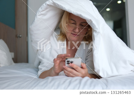 bed robe Relaxing woman in a robe using phone on a bed at a cozy hotel room Woman in a white robe using a smartphone while sitting on a bed in a cozy, well-decorated bedroom. bed robe Relaxing woman in a robe using phone on a bed at a cozy hotel room Woman in a white robe using a smartphone while sitting on a bed in a cozy, well-decorated bedroom. 131265463