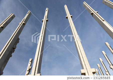 Tall concrete pillars rise against blue sky, forming structural framework of unfinished building. The perspective view emphasizes height, strength and the modern industrial character of construction 131265685