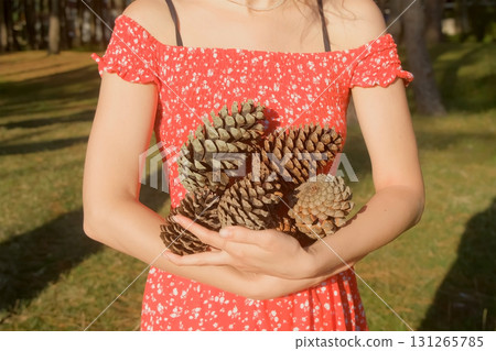 Unrecognizable woman in red dress holding pine cones in sunny forest. Unrecognizable woman in red dress holding pine cones in sunny forest. 131265785