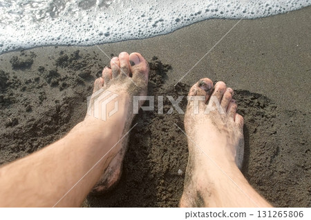 Barefooted man legs on sandy volcanic beach: gentle waves washing over feet. Barefooted man legs on sandy volcanic beach: gentle waves washing over feet. 131265806