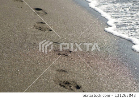 Gentle waves washing away human footprints on black sandy sea beach. 131265848