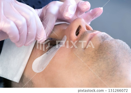 Cosmetologist removing curlers from man's eyes after lash laminating procedure. Cosmetologist removing curlers from man's eyes after lash laminating procedure. 131266072