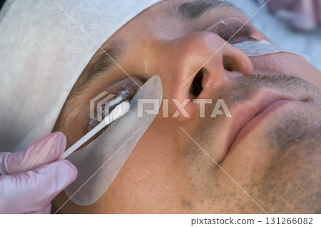 Woman applies solution on man's eyelashes for laminating lifting lash procedure. Woman applies solution on man's eyelashes for laminating lifting lash procedure. 131266082