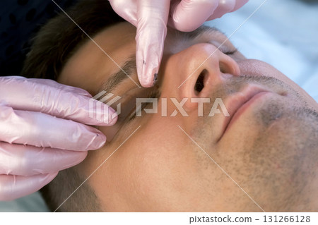 Beautician installing curler on man's eyelid for eyelash lifting and laminating. Beautician installing curler on man's eyelid for eyelash lifting and laminating. 131266128