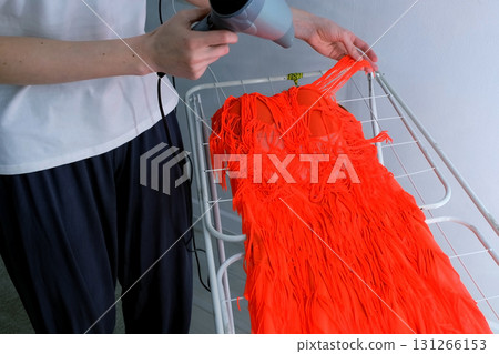 Woman is drying dress for sports ballroom dancing using hair dryer, closeup. 131266153