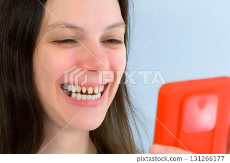Young smiling woman with yellow bad teeth calling by video on mobile phone. Young smiling woman with yellow bad teeth calling by video on mobile phone. 131266177