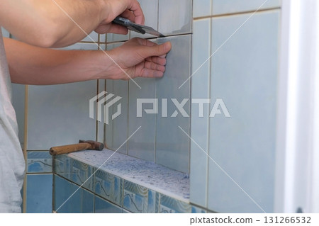 Man tiler making renovation repair at home, removes tiles from wall in toilet. Man tiler making renovation repair at home, removes tiles from wall in toilet. 131266532