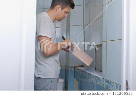 Man tiler making renovation repair at home, removes tiles from wall in toilet. Man tiler making renovation repair at home, removes tiles from wall in toilet. 131266533
