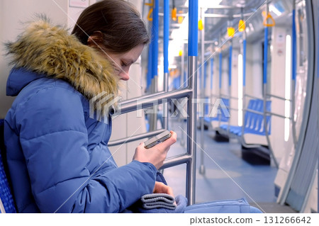 Woman goes in an empty subway car and watches a video on her smartphone. Side view. Woman goes in an empty subway car and watches a video on her smartphone. Side view. 131266642