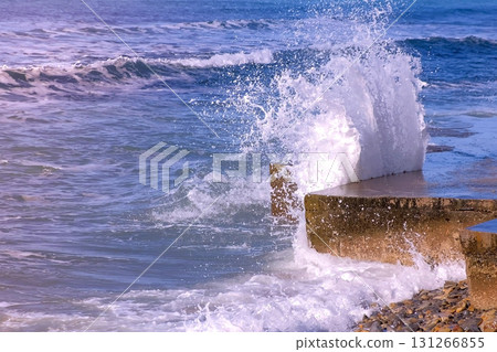 Splashes of water from the stormy waves breaking on the breakwater on waterfront. Side view. 131266855