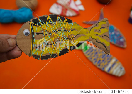 Construct a fish figure from cardboard, thread, and paint, with detailed steps, set against an orange background. Construct a fish figure from cardboard, thread, and paint, with detailed steps, set against an orange background. 131267724