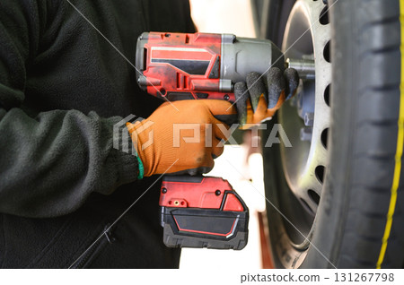 A close-up shot of a mechanic using an electric impact wrench to remove a car wheel A close-up shot of a mechanic using an electric impact wrench to remove a car wheel 131267798