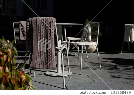 Chic outdoor cafe terrace with modern seating, perfect for business meetings or casual gatherings. Stylish minimalist furniture and cozy blanket set scene for productive and comfortable outdoor work Chic outdoor cafe terrace with modern seating, perfect for business meetings or casual gatherings. Stylish minimalist furniture and cozy blanket set scene for productive and comfortable outdoor work 131268489