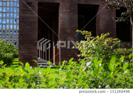 Modern residential building with brick facade and lush greenery in foreground. Captures the harmony between urban architecture and nature, with clean lines and natural elements blending seamlessly 131268496
