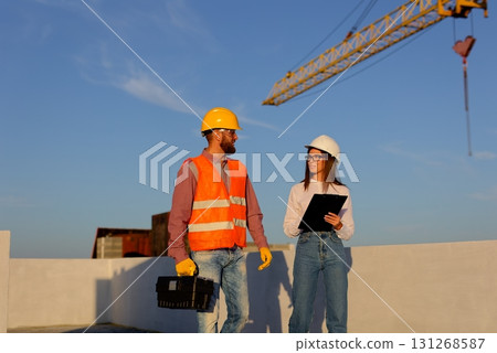 Construction workers discussing blueprint on building site with crane in background 131268587